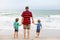 Two happy little kids boys and father standing on the beach of ocean and looking on horizon on stormy day. Family, dad