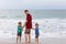 Two happy little kids boys and father standing on the beach of ocean and looking on horizon on stormy day. Family, dad