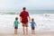 Two happy little kids boys and father standing on the beach of ocean and looking on horizon on stormy day. Family, dad