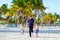 Two happy little kids boys and father walking on the beach of ocean with palms on sunny day. Family, dad and cute