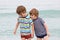 Two happy little kids boys running on the beach of ocean. Funny children, siblings, twins and best friends making