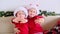 Two happy little sisters children kids in Santa Claus hat waves hands and looking into the camera.