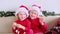 Two happy little sisters children kids in Santa Claus hat waves hands and looking into the camera.