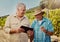 Two happy senior farmers standing and talking while using a digital tablet on their vineyard. Smiling elderly men and