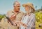 Two happy senior farmers standing and talking while using digital tablet on a vineyard. Smiling elderly man and woman