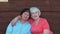 Two happy senior women hugging and singing together near wooden wall