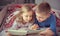 Two happy sibling children reading book in bunk bed under blanket