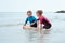 Two happy siblings children in neoprene swimsuits playing with sand in sea