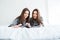 Two happy sisters twins lying on bed and reading magazine