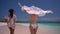 Two happy slim girls in beach tunics are running along a pink sand beach, one girl waves her arms like white wings