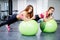 Two happy sportswomen exercising with a ball doing plank exercise in gym.