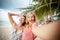 Two happy young beautiful girlfriends laugh make selfie on the background of palm trees and tropical sea, travel and holidays