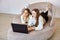 Two happy young sisters lie on sofa with laptop.