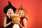 Two happy young women in black and red dresses, costumes witches halloween on party over orange background. Festive