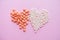 Two hearts made of homeopathic globules and orange pills on pink background. Homeopathy medicine, healtcare, Epidemic, painkillers