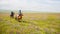 Two herdsmen ride horses on meadows.