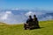 Two hikers sitting on the bench and enjoying the beautiful view of the cloudy sky