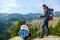 Two hikers at viewpoint in the mountains enjoying beautiful view of the valley with a lake.