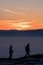 Two hikers walking on mountain over low stratus to sunset