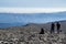 Two hikers walking on slate ground descending from the top of Mulhacen, then a plain crossed by a path, then a mountain range and