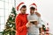 Two hispanic men couple looking photo hugging each other standing by christmas tree at home