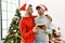 Two hispanic men couple looking photo hugging each other standing by christmas tree at home