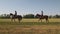 Two horsewomen are riding horses along a grassland