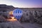 two hot air balloons full of tourists, about to take off at dawn between fairy chimneys, service vans around the balloons,