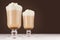 Two hot coffee drinks with whipped cream in wineglass in dark brown interior on white wooden table, copy space.
