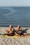 Two hot slim dark-haired girls in swimsuits lay on the yellow surfboard on the sandy beach near the sea on a sunny day.