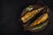 Two hot smoked herrings with ropes and spices lie on a clay plate on a black board and a black background. view from above. dark