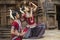 Two Indian classical odissi dancers striking pose against the backdrop of Mukteshvara Temple with sculptures in bhubaneswar, Odish