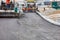 Two industrial pavers apply the first layer of hot asphalt on a new stretch of road