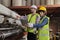 Two industrial workers use a laptop to check a paper manufacturing machine