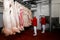 Two inspectors in red and white overalls checking the quality of the pieces of pork in the factory. Horizontal view.
