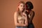 Two international girls in beige bra, african and european girls looking at the camera  over dark orange