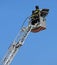 Two intrepid firefighters over the ladder truck metal basket