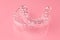 Two Invisible dental teeth aligners on the pink background. Orthodontic temporary removable braces for fixing teeth