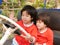 Two ittle Asian baby girls, sisters, holding on a steering wheel and pretending to drive a parking car