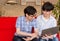 Two Japanese young men talking about contents on the internet, sitting on sofa at home