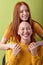 two Joyful young bald and redhead women hugging posing isolated on green background