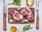Two juicy fresh raw pork steak on a cutting board, with butter, herbs, knife and fork on wooden rustic background top view close u