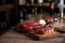 Two juicy, fresh striploin steaks in a grill pan and ribeye steak on a cutting board on a countertop and barrel boards with tomato