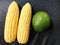 Two jumbo sized corn and avocado on black leather board