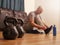 Two kettle bells in focus. Bald man fixing his shoes sitting on the floor of living room out of focus.