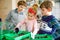 Two kid boys and little toddler girl planting vegetable seeds at home. Three siblings watering together ground in boxes