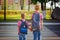 Two kids with backpacks walking on the road, holding. School tim