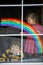 Two kids, school boy and toddler girl with rainbow painted with colorful window color during pandemic coronavirus