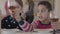 Two kids sitting at the table at home. Caucasian blond girl and african american boy have fun together. The boy giving