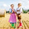 Two kids in traditional Bavarian costumes in wheat field. German children eating bread and pretzel during Oktoberfest